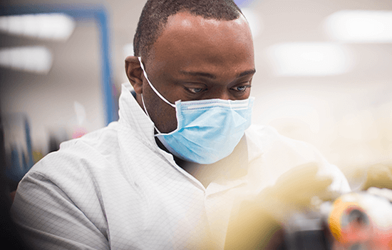 Homem com uma máscara, de bata, trabalha num laboratório