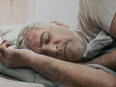 Homem deitado de lado numa cama de olhos fechados